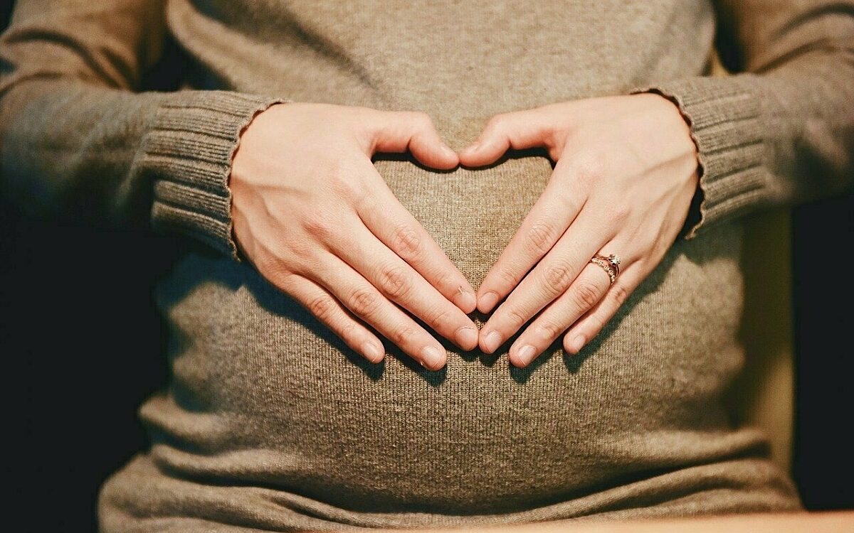 Eine Schwangere hält ihre Hände zu einem Herz geformt vor den Bauch Eine Schwangere hält ihre Hände zu einem Herz geformt vor den Bauch